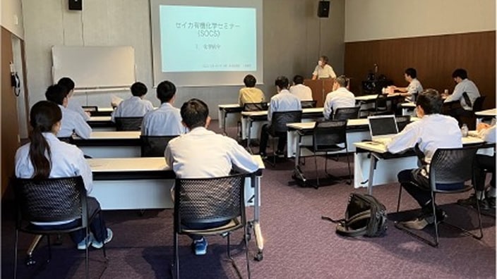 スクリーンに「セイカ有機化学セミナー（SOCS）」と映し出された講義を、新入社員たちが受講している写真