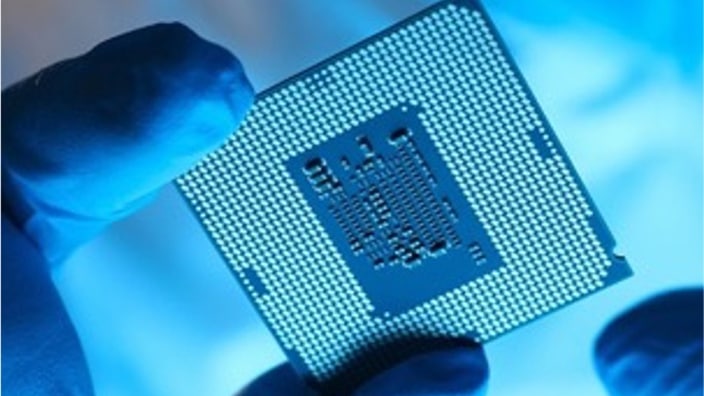 作業用手袋をした手で、接点が並んだ半導体チップを持っている写真。背景は青白い光に包まれている