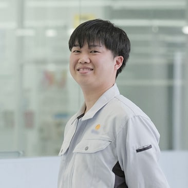 研究部 Nさんの写真。ユニフォームを着用し、笑顔を浮かべている。背景には実験器具が並んだ部屋が映り込む