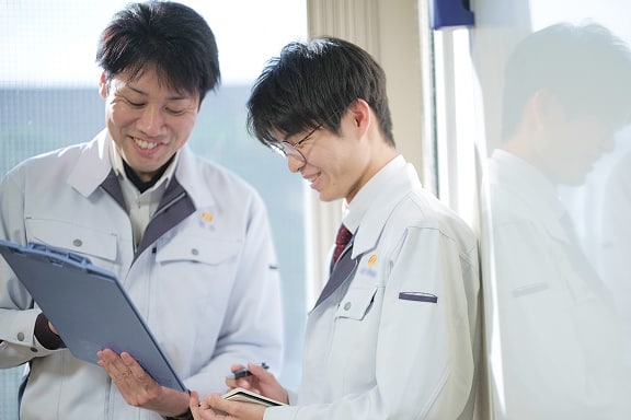 和やかに談笑するふたりの社員の写真。1人は手に持ったクリップボードを指さし、もう1人はメモを取っている