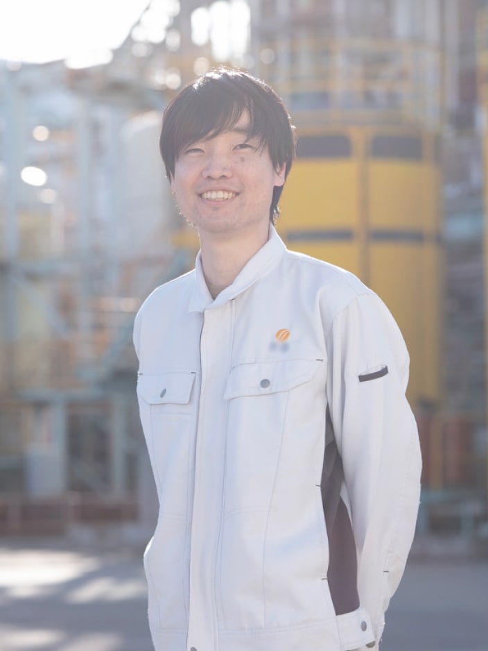 2018年度入社 生産技術部 R.Sさんの写真。ユニフォームを着用している。背景には工場の機械や配管が映り込む