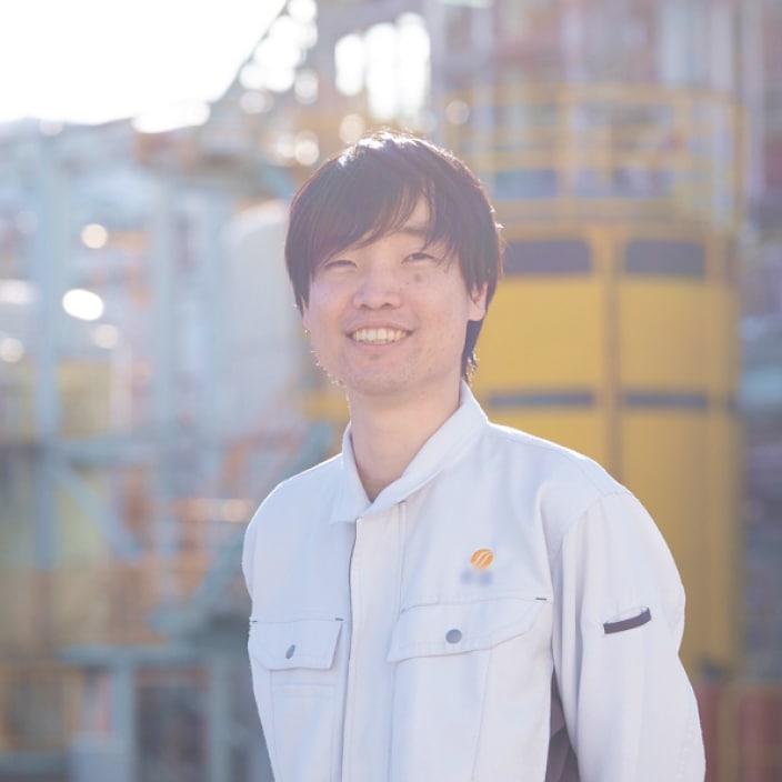 2018年度入社 生産技術部 R.Sさんの写真。ユニフォームを着用している。背景には工場の機械や配管が映り込む