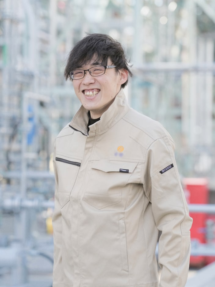 2017年度入社 製造部 S.Yさんの写真。ユニフォームを着用している。背景には工場の配管が映り込む