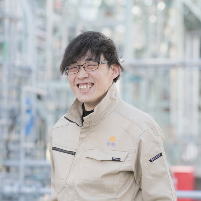 2017年度入社 製造部 S.Yさんの写真。ユニフォームを着用している。背景には工場の配管が映り込む