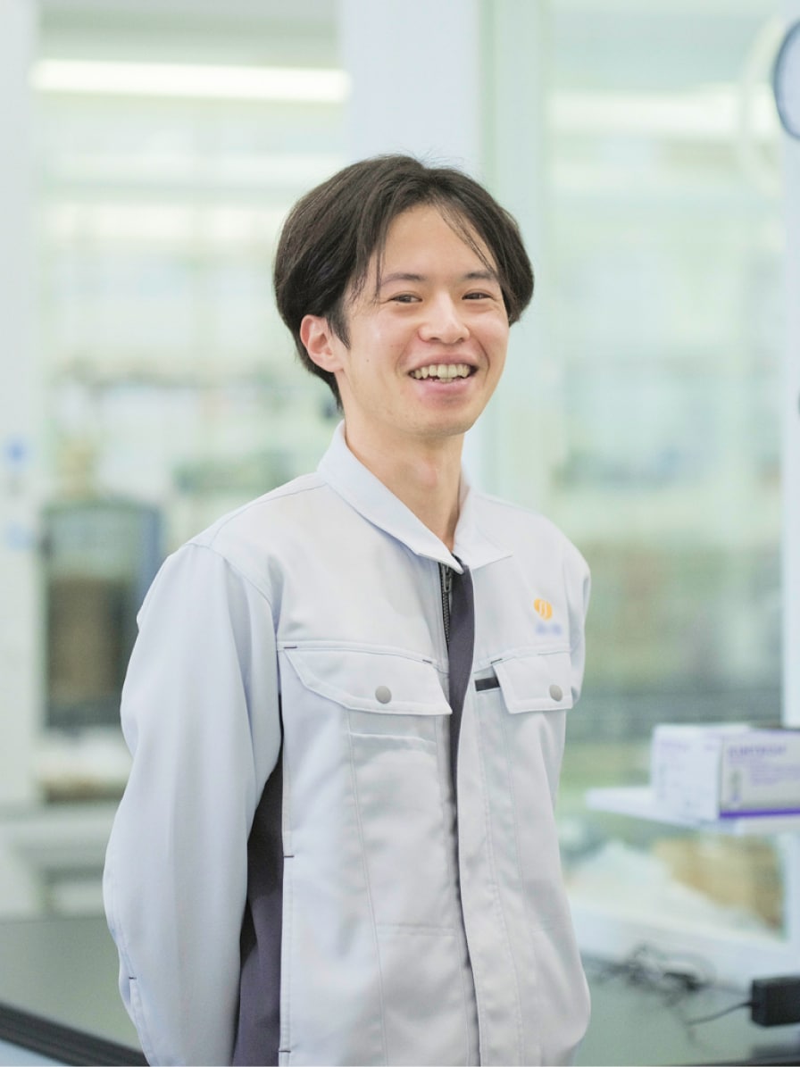 2021年度入社 研究部 Y.Yさんの写真。背景には実験器具が並んだ部屋が映り込む
