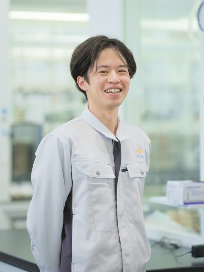 2021年度入社 研究部 Y.Yさんの写真。背景には実験器具が並んだ部屋が映り込む