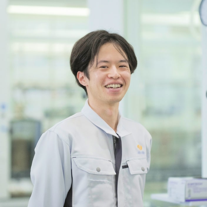2021年度入社 研究部 Y.Yさんの写真。背景には実験器具が並んだ部屋が映り込む