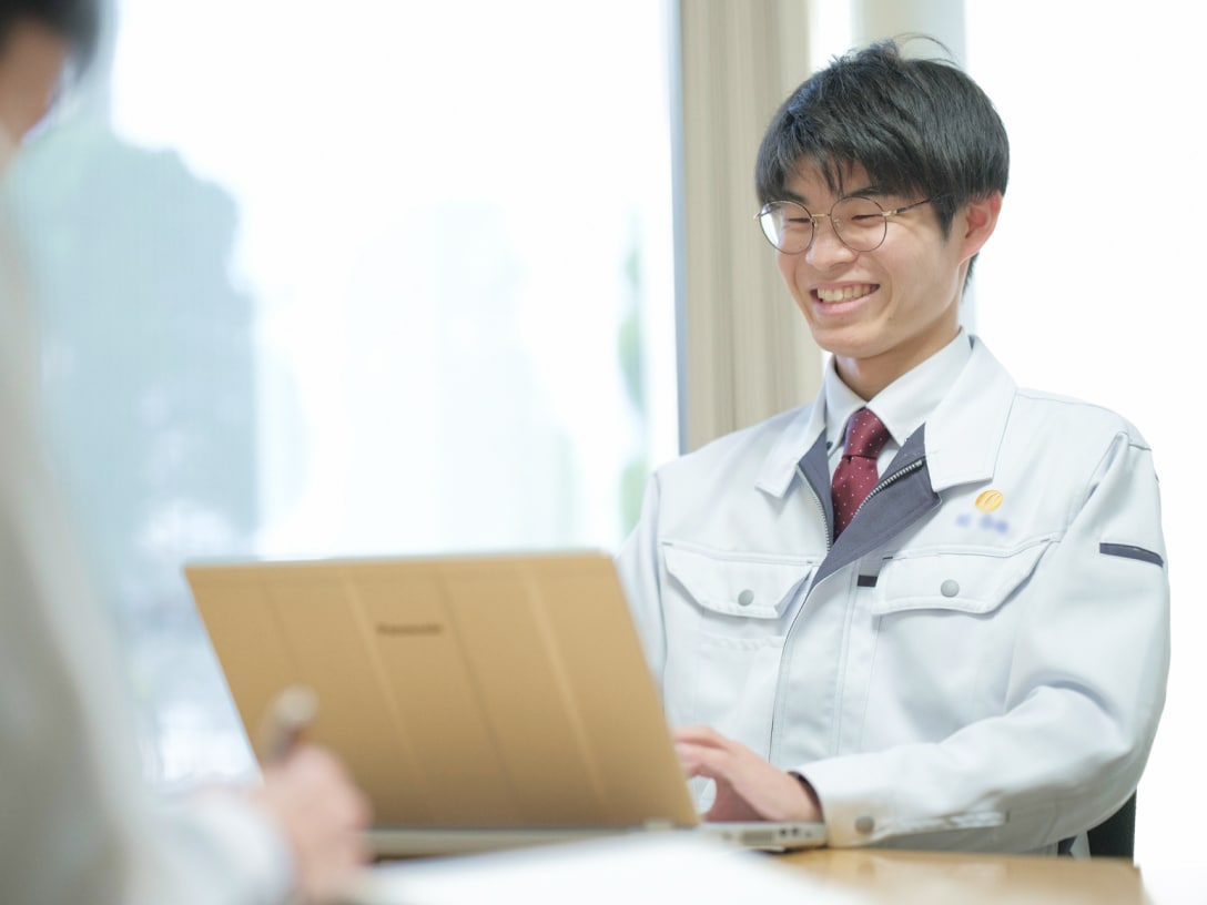 ノートパソコンを見ながら、向かいの人物と笑顔で話しているT.Tさんの写真